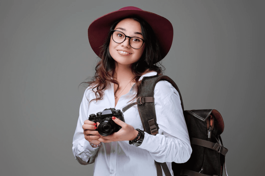 beautiful woman photographer wearing a white shirt and a red hat holding a camera in her hands